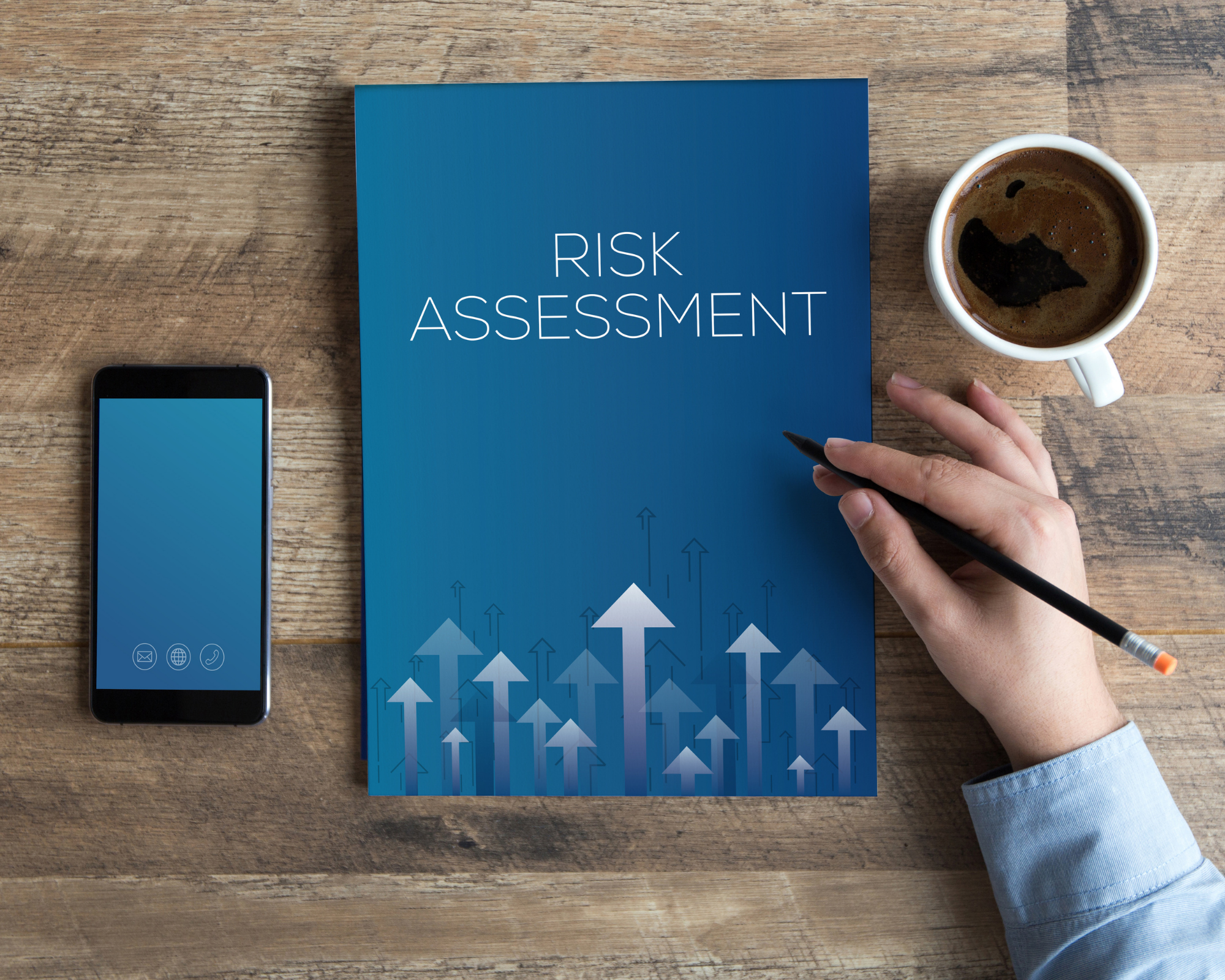 Image of a blue risk assessment folder on a table, next to a phone, a coffee and someone's arm.