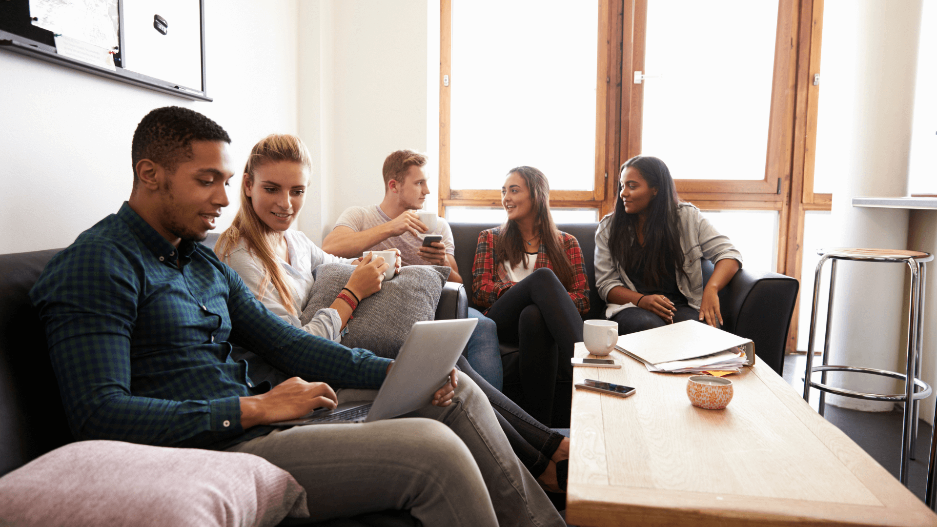Students sitting around a table in a living room, talking and looking at a laptop