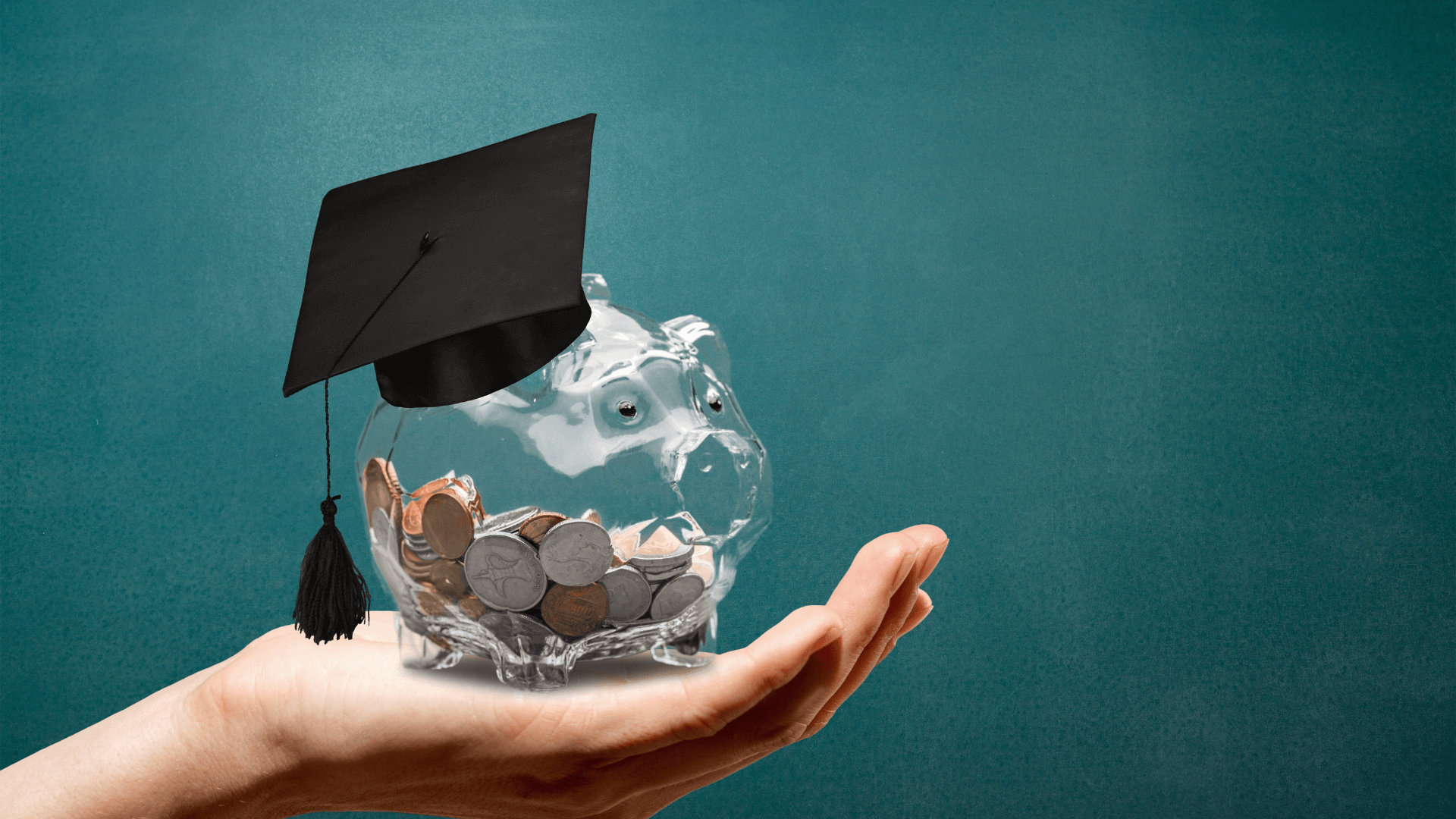 Hand holding a piggy bank wearing a graduation cap